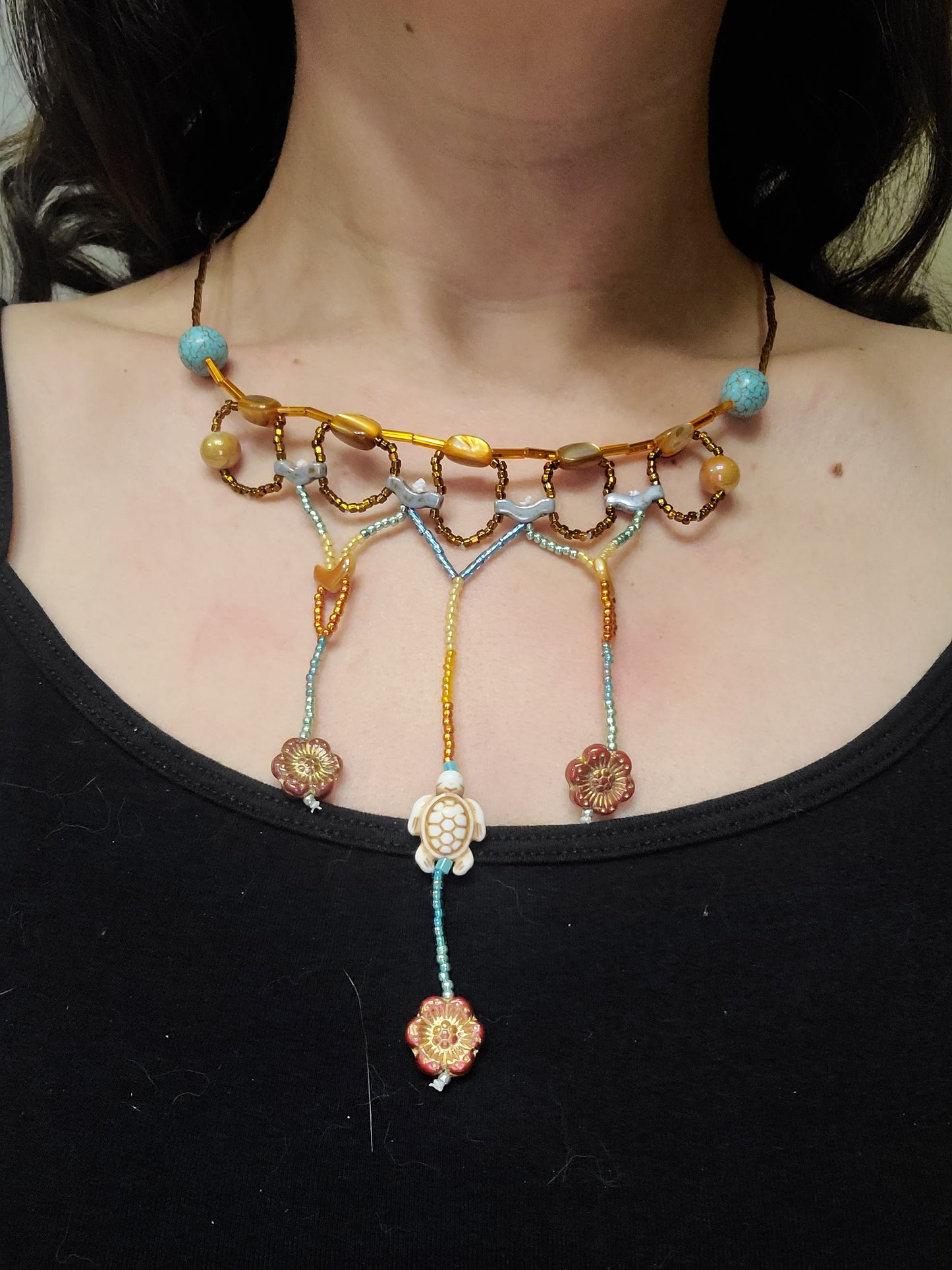 Model wearing an autumn statement necklace featuring interlocking circles and three dangles with statement beads, including floral glass beads and a howlite turtle bead.