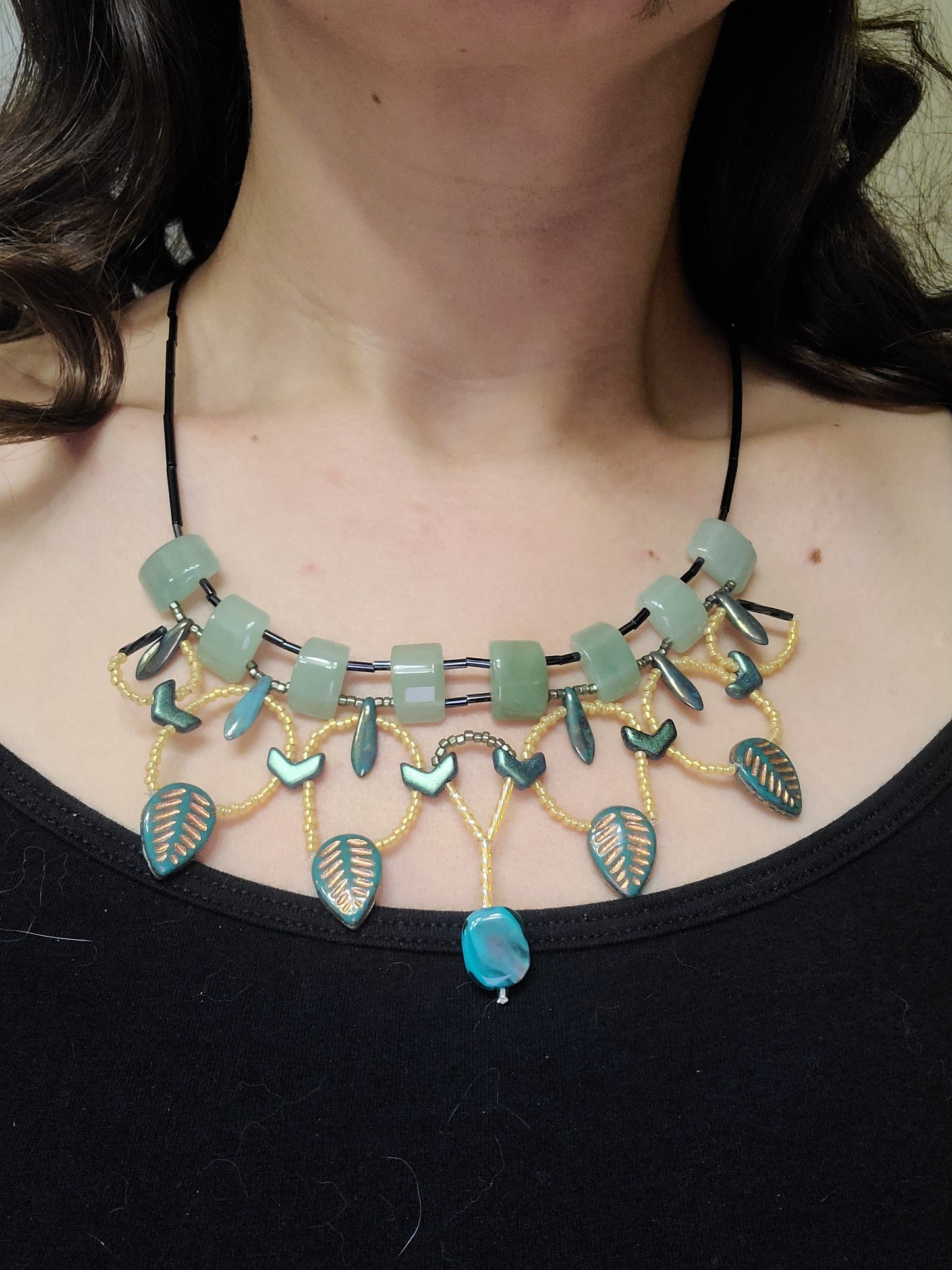 Model wearing an aventurine necklace with gold and teal leaf beads and an aqua blue bead at the center.
