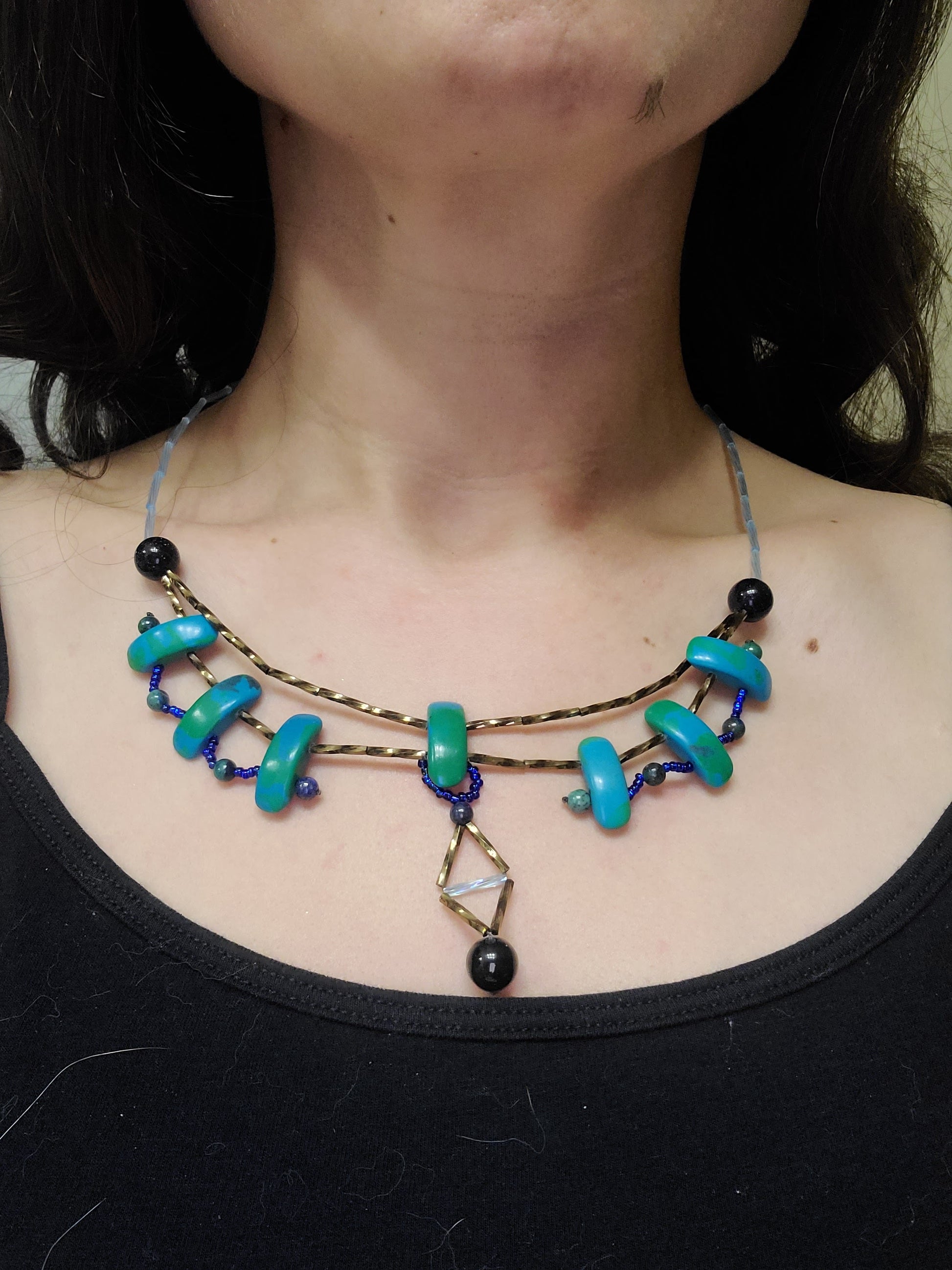 Model wearing a Y-shaped dramatic necklace with blue and green azurite beads with a delicate dangle at the center with dark agate beads.