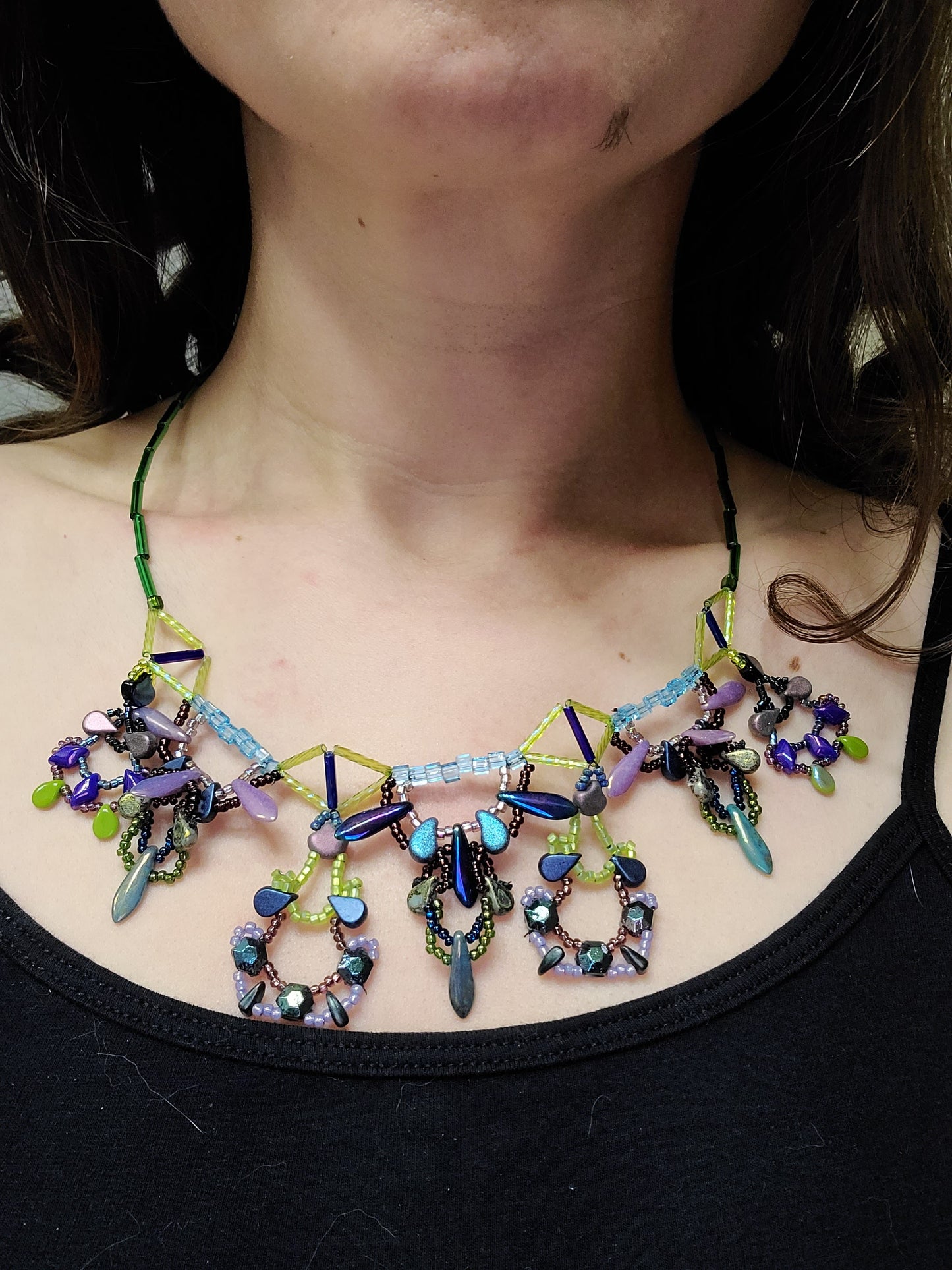 Dark-haired woman wearing purple, lime, and teal beaded necklace.