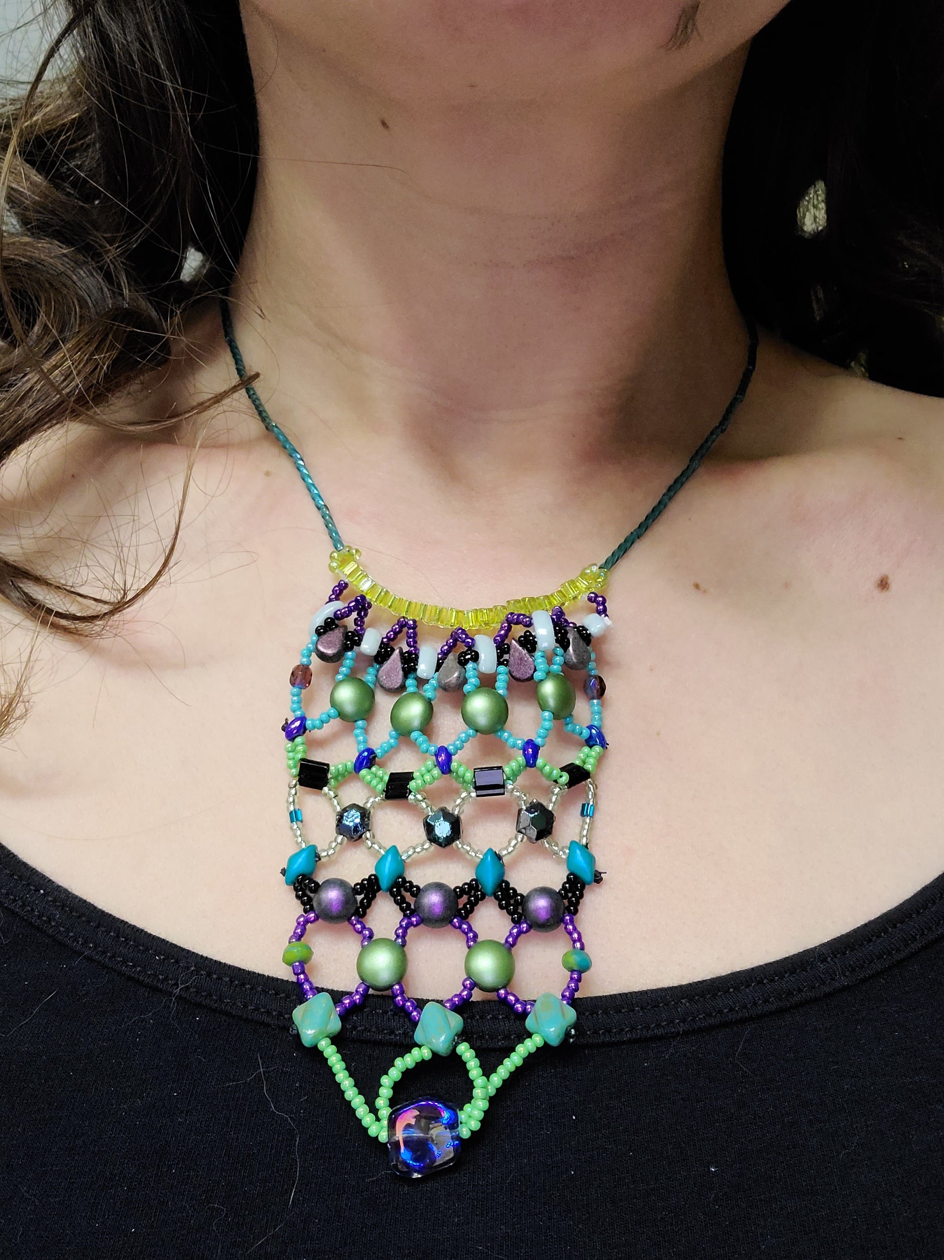 Dark-haired woman wearing purple, teal and lime statement necklace.