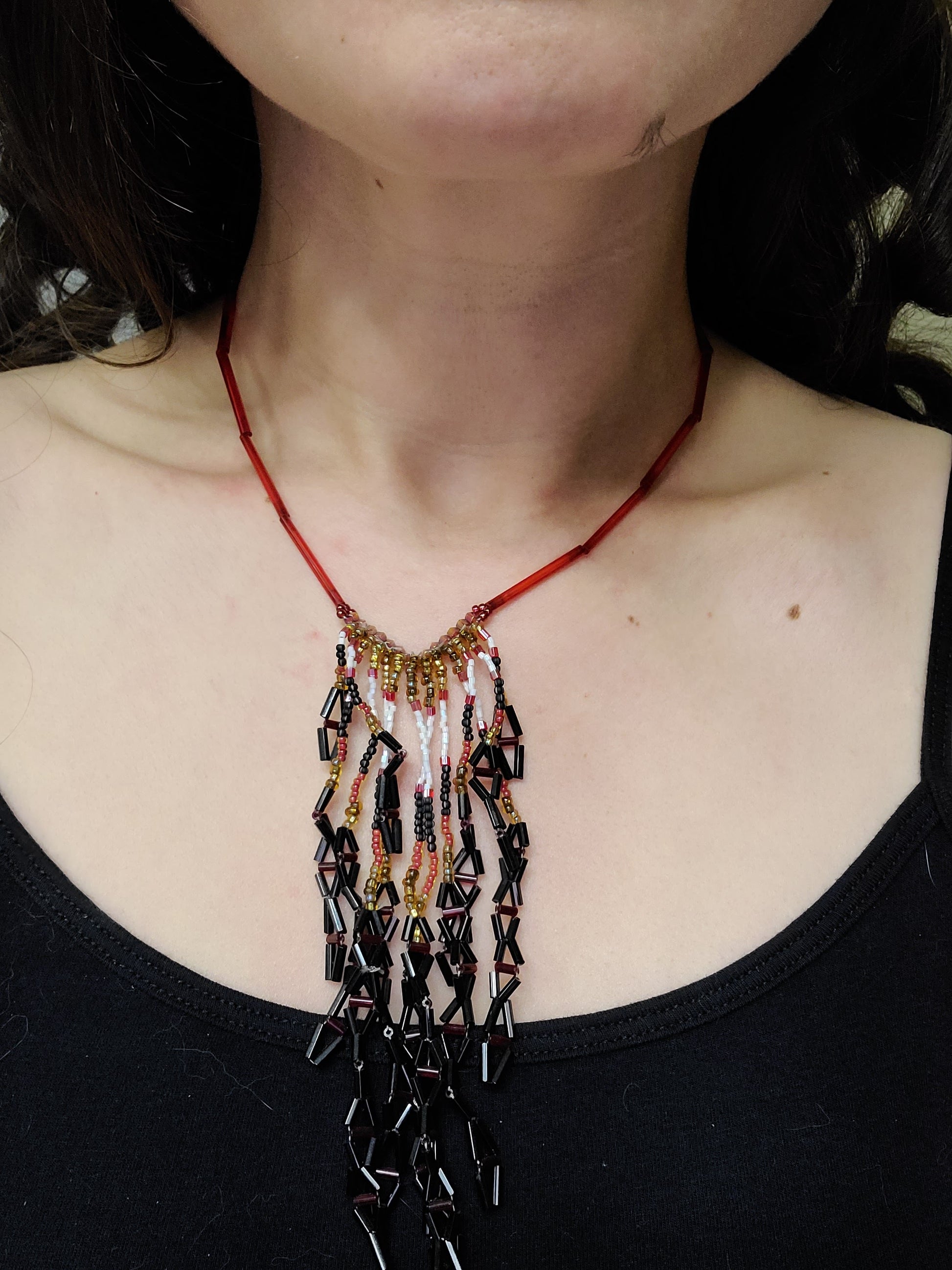 Dark-haired woman wearing red, black, gold, and white diamond fringe necklace.