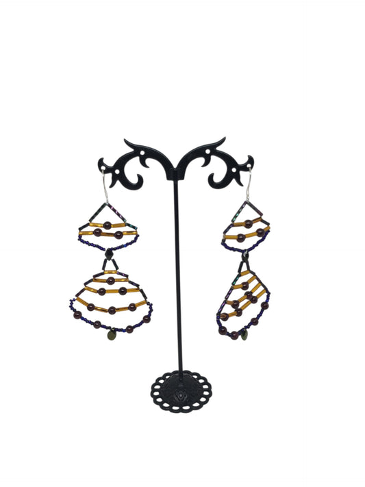 Stacked teardrop drop earrings with deep red pyrope garnet rounds, blue-violet iridescent frames, amber gold glass tubes, and pale glass teardrop drop.