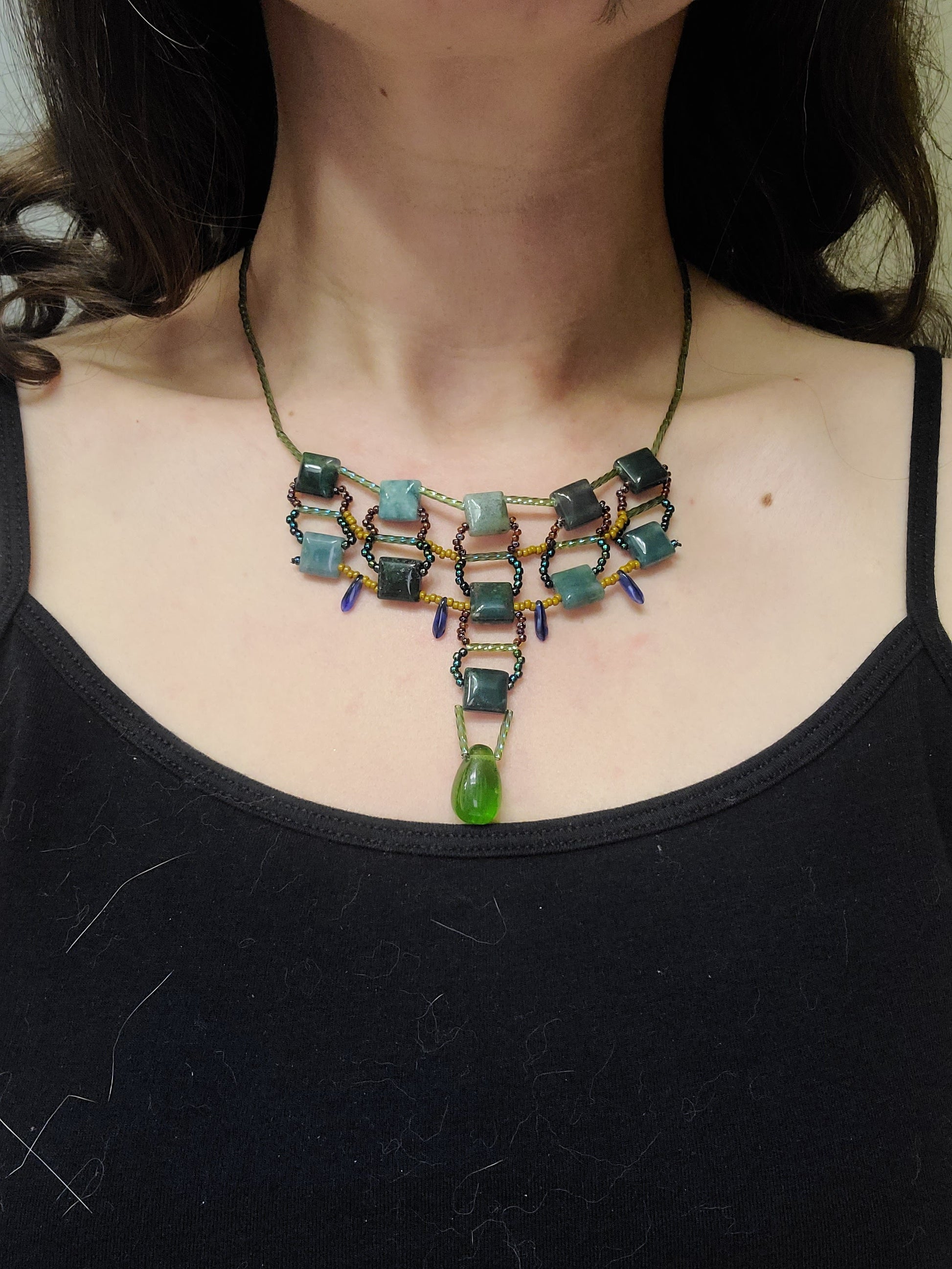 Dark-haired woman wearing moss agate statement necklace. 